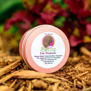 Bonitas Loc Pomade in a round pink metal tin, photographed against flowers